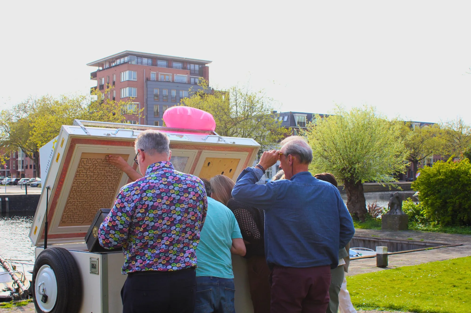 Een groep spelers puzzelt rond de opengeklapte mobiele escaperoom van Escape Tour, met een roze flamingo op het dak